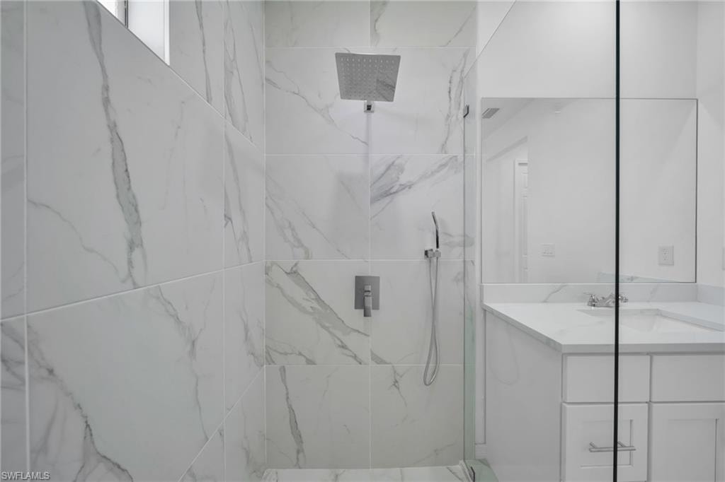 Glass-enclosed shower with large format tile walls, rainfall showerhead, and wall-mounted controls