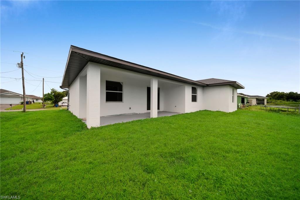 White stucco exterior with a covered patio, dark roof, and substantial grassy yard(ENHANCED GRASS COLOR FOR VISIBILITY)