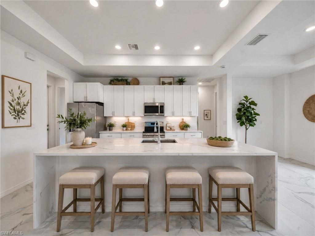 AI: Example of Contemporary kitchen featuring white shaker-style cabinetry, stainless steel appliances, and a waterfall-edge island with stone countertops
