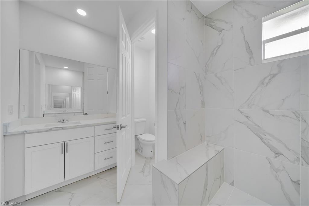 White vanity with integrated sink, expansive wall mirror, recessed lighting, and large format veined tile