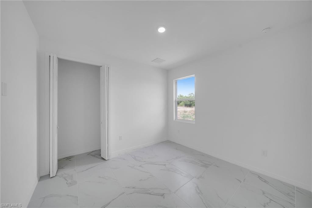 GUEST BEDROOM 2: Bright corner bedroom featuring polished stone-finish flooring, abundant natural light from dual windows, and clean white walls with recessed ceiling lighting