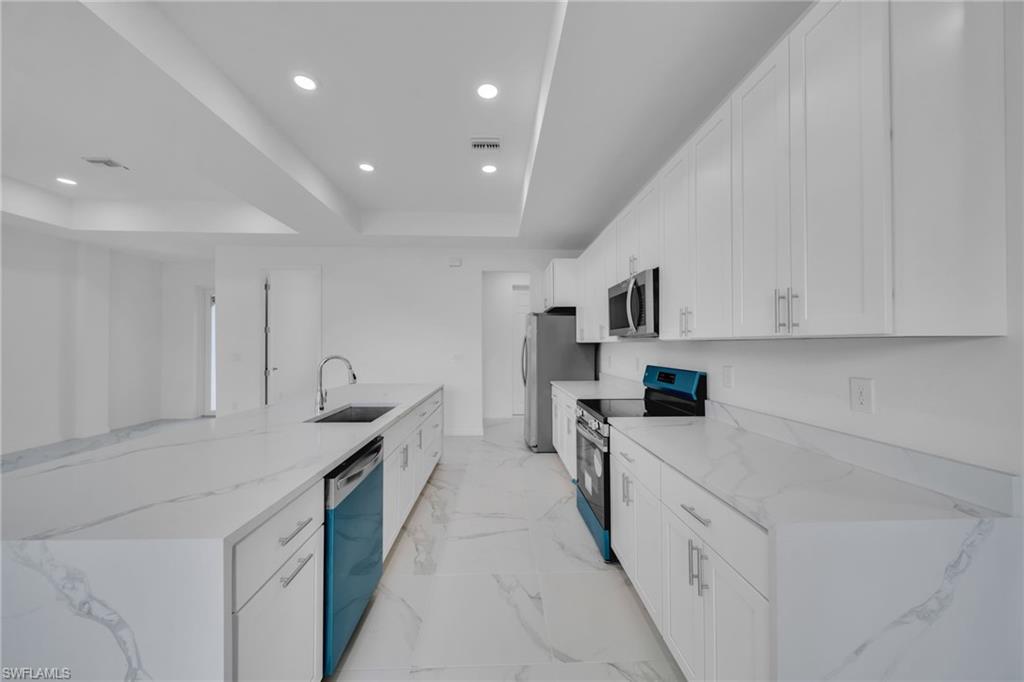 Modern kitchen featuring white cabinetry with soft-close hardware, quartz countertops with veining throughout, stainless steel appliances including a built-in refrigerator and dual ovens, an undermount sink with a gooseneck faucet, and recessed ceiling lighting with coffered detail