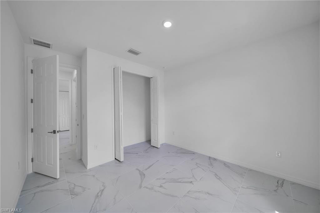 GUEST BEDROOM Bright, open bedroom with elegant marble-look flooring, recessed ceiling lighting, and multiple white panel doors providing access to adjoining spaces