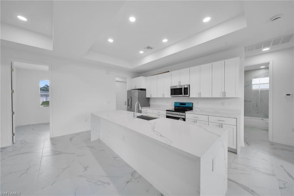 White shaker cabinetry, stainless steel appliances, large kitchen island with integrated sink, white stone countertops, and tile flooring