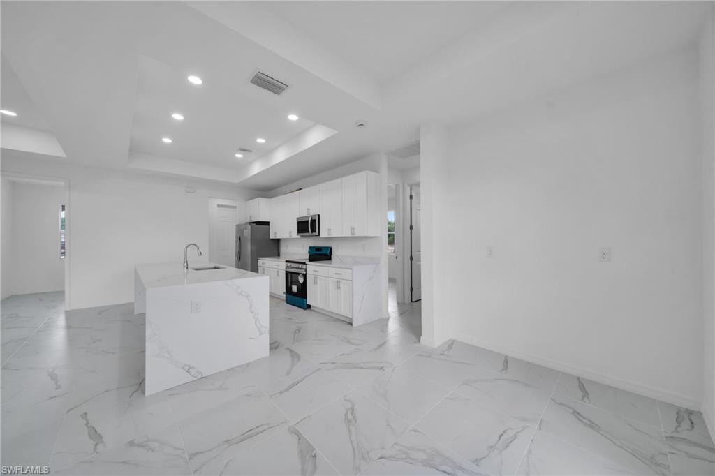 Kitchen featuring an island with an integrated sink, white cabinetry, stainless steel appliances, and large format tile flooring