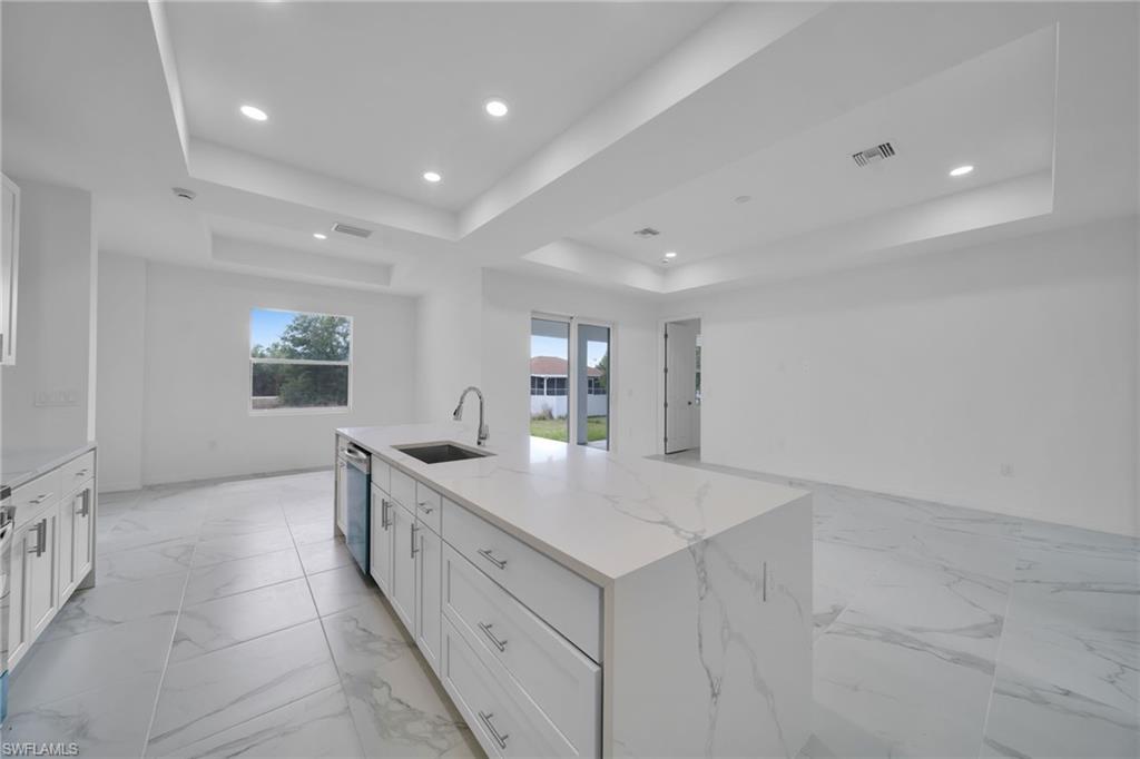 White shaker cabinetry with chrome hardware, waterfall-edge countertop, stainless steel sink with pull-down faucet, recessed lighting, and tile flooring