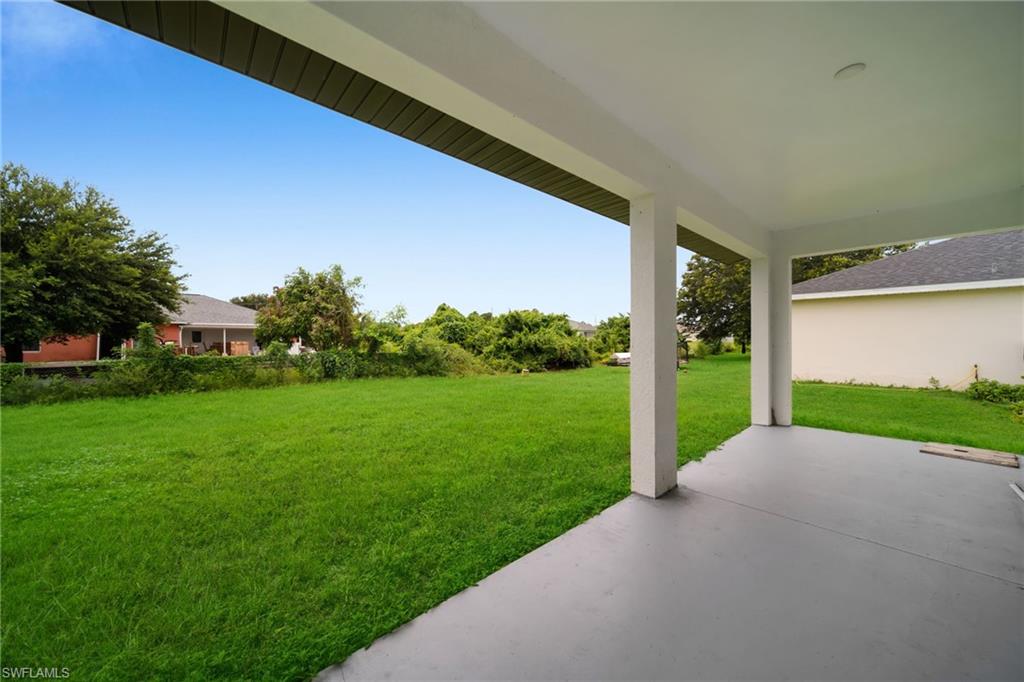 Covered patio with a concrete surface, supported by white columns, overlooking a spacious green lawn (ENHANCED GRASS COLOR)