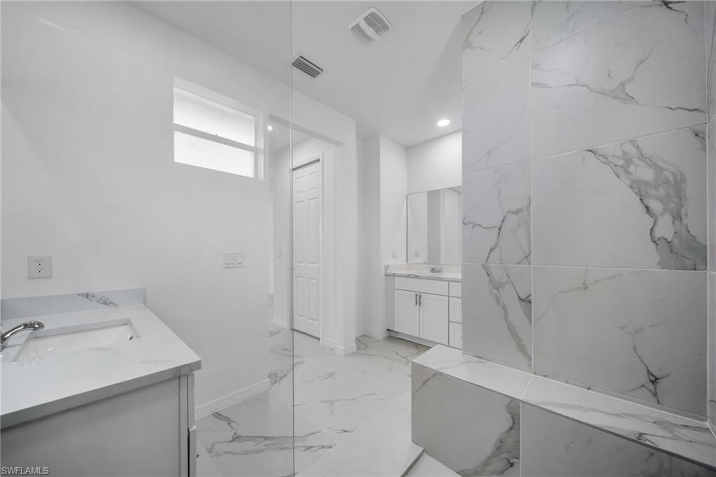 Spa-inspired primary bathroom featuring marble-look porcelain tile flooring and wall cladding, dual vanity with white cabinetry and quartz countertop, frameless glass shower enclosure, and recessed ceiling lighting