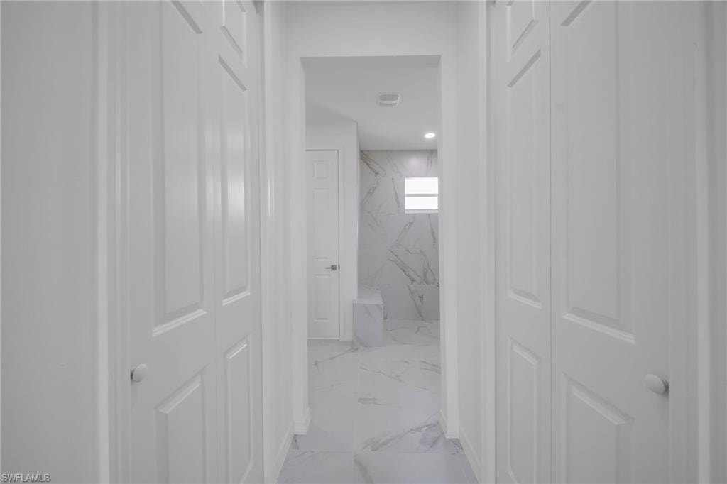 Hallway featuring two sets of white bi-fold doors, white interior walls, and a tiled floor extending into an additional space with a small rectangular window