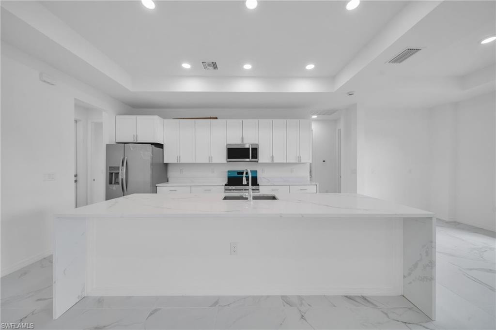 Spacious kitchen featuring an expansive island with an undermount sink, white cabinetry, stainless steel appliances, and tile flooring