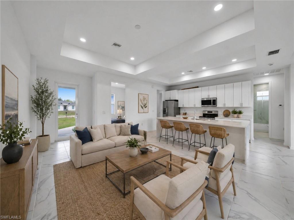 AI: EXMAMPLE: Open-concept living and kitchen featuring polished stone flooring, recessed ceiling lighting, white cabinetry with integrated appliances, wood-finish bar-height seating for three, and expansive windows overlooking the exterior grounds
