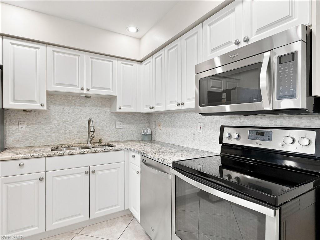 White cabinetry with silver-tone hardware, textured tile backsplash, stainless steel appliances, granite-finish countertops, and recessed lighting