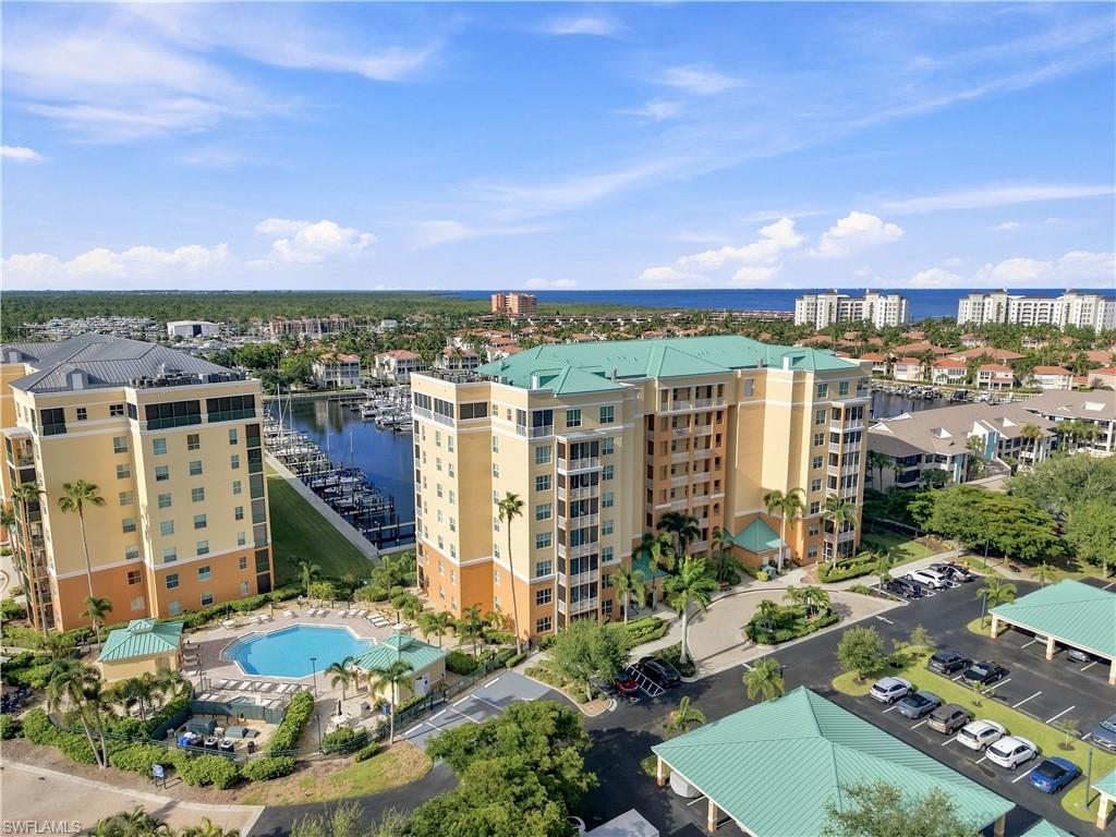 Expansive building featuring a large swimming pool, marina access, lush landscaping, covered parking, and ocean scenery