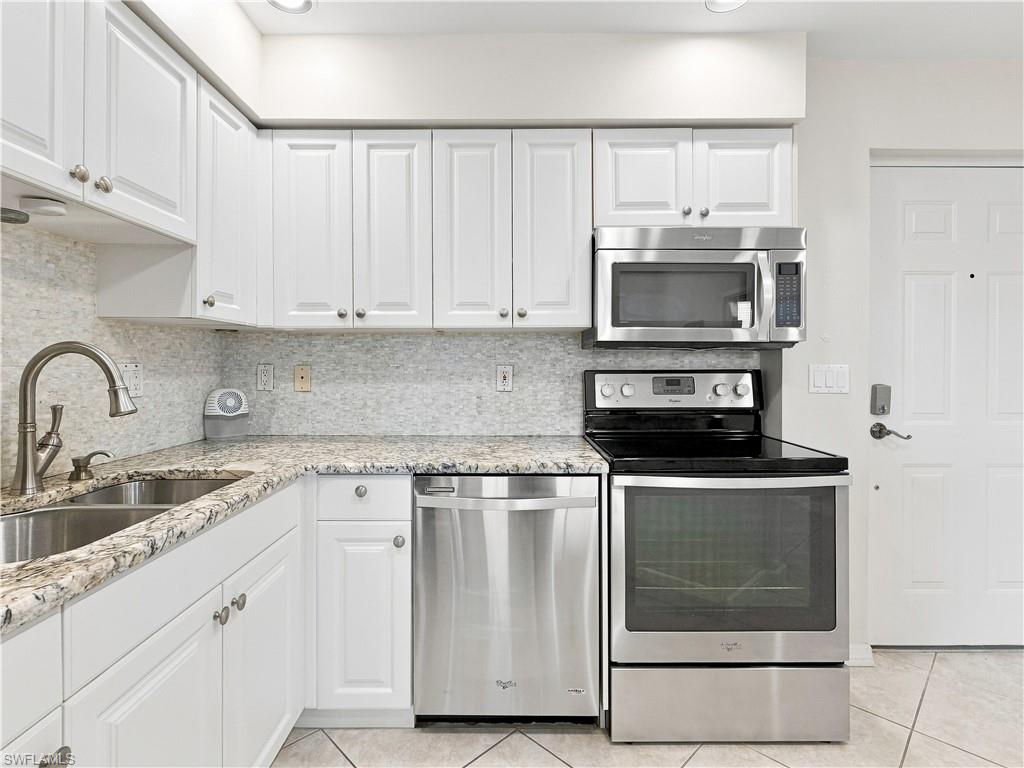 White shaker-style cabinetry, stainless steel appliances, granite-finish countertops, tile backsplash, and a double basin stainless steel sink