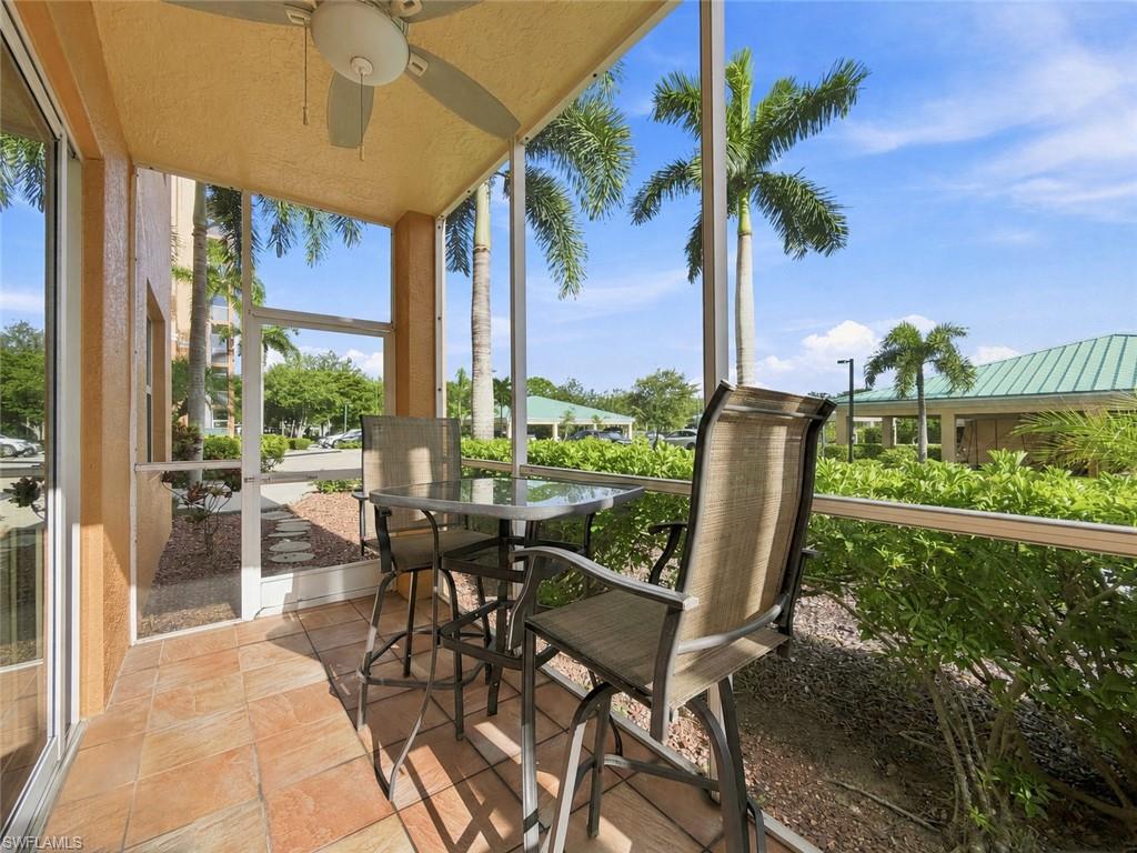 Screened porch featuring a ceiling fan, terracotta-style tiled flooring, and mature palm trees