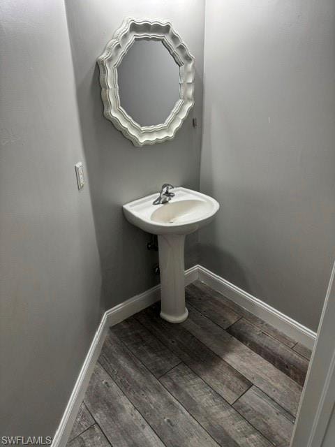 Pedestal sink with chrome faucet, decorative framed mirror, and wood-finish flooring