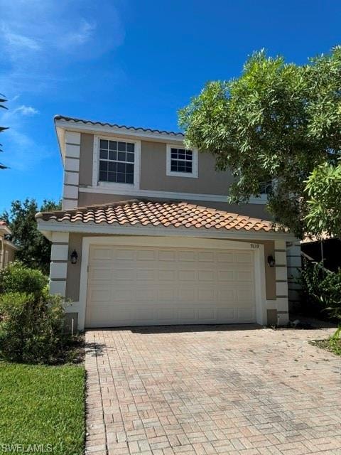 Light-toned exterior with a tile roof, an integrated garage, and a paver driveway