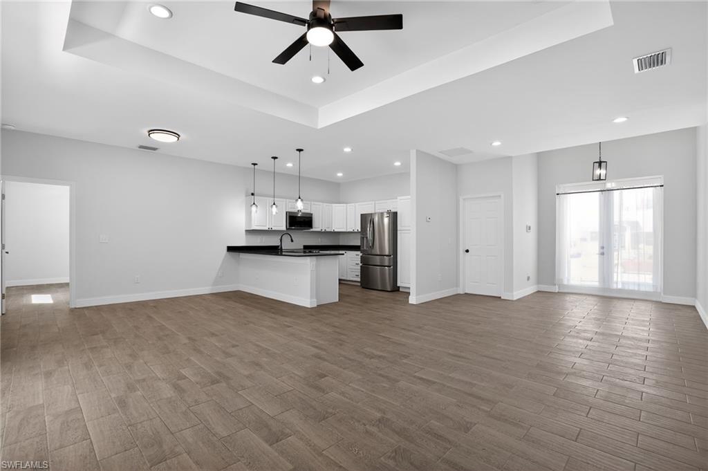 Tray ceiling with a ceiling fan, recessed lighting, wood-finish flooring, white cabinetry, and stainless steel appliances