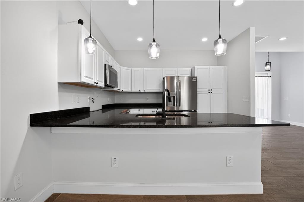 Kitchen featuring white cabinetry, stainless steel appliances, dark countertops, and pendant lighting