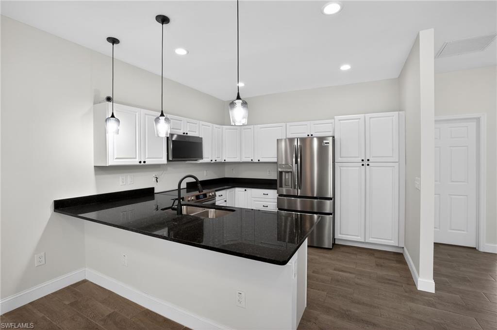 Kitchen featuring white cabinetry, dark stone countertops, stainless steel appliances, and wood-finish flooring