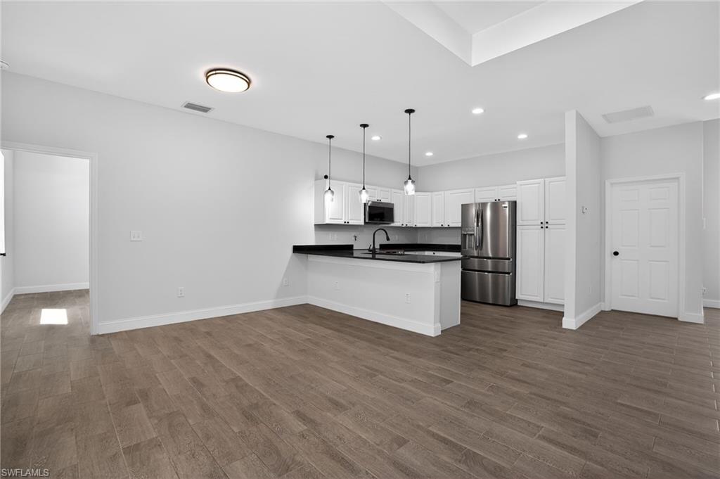 Open-concept layout with wood-finish flooring, white cabinetry, and stainless steel appliances