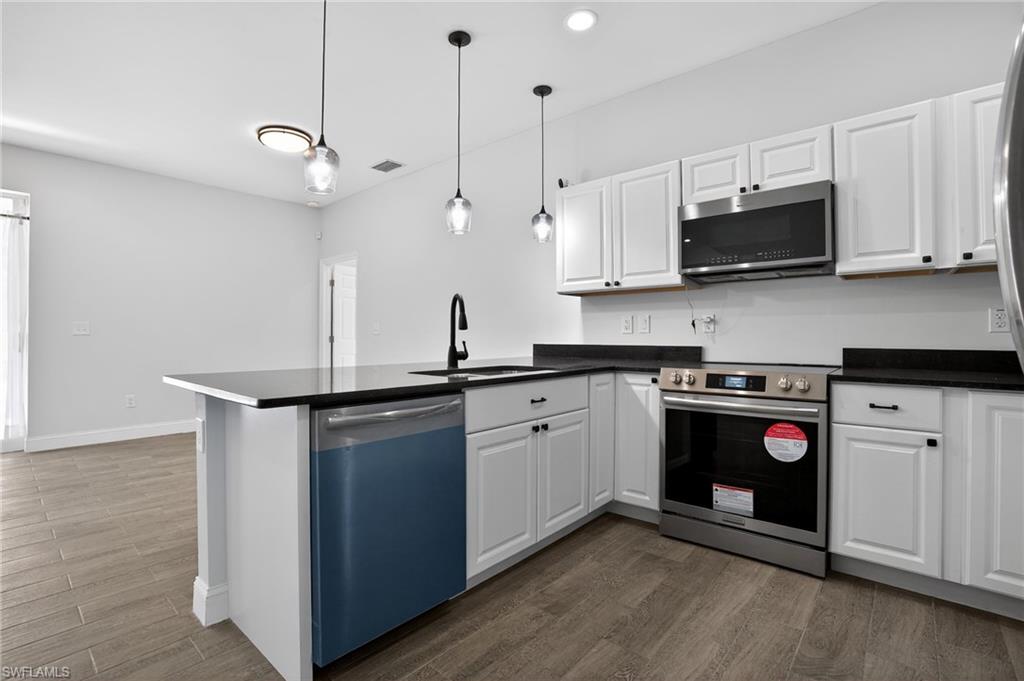 Kitchen featuring white shaker-style cabinetry, black countertops, stainless steel appliances, and wood-finish flooring