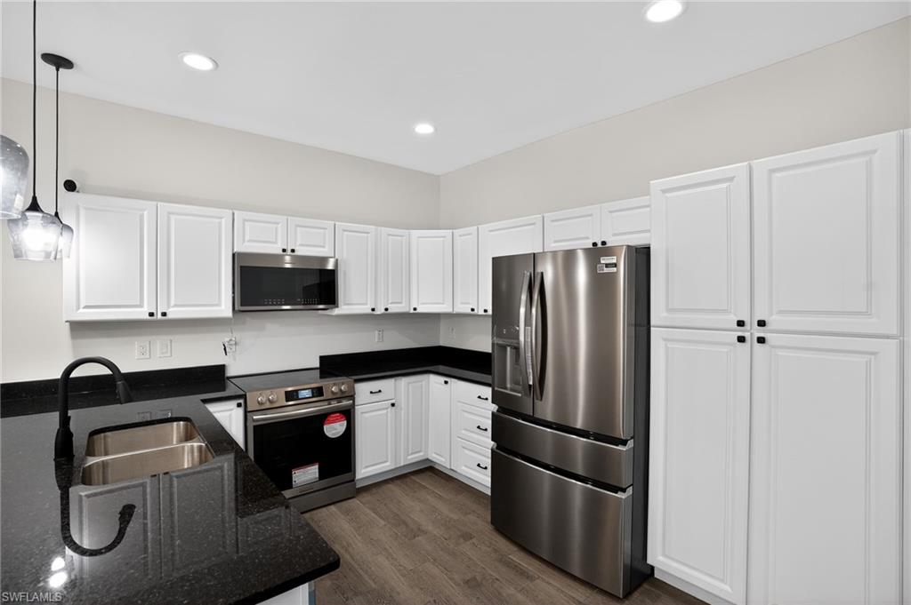 Contemporary kitchen featuring white cabinetry, dark countertops, stainless steel appliances, and wood-finish flooring
