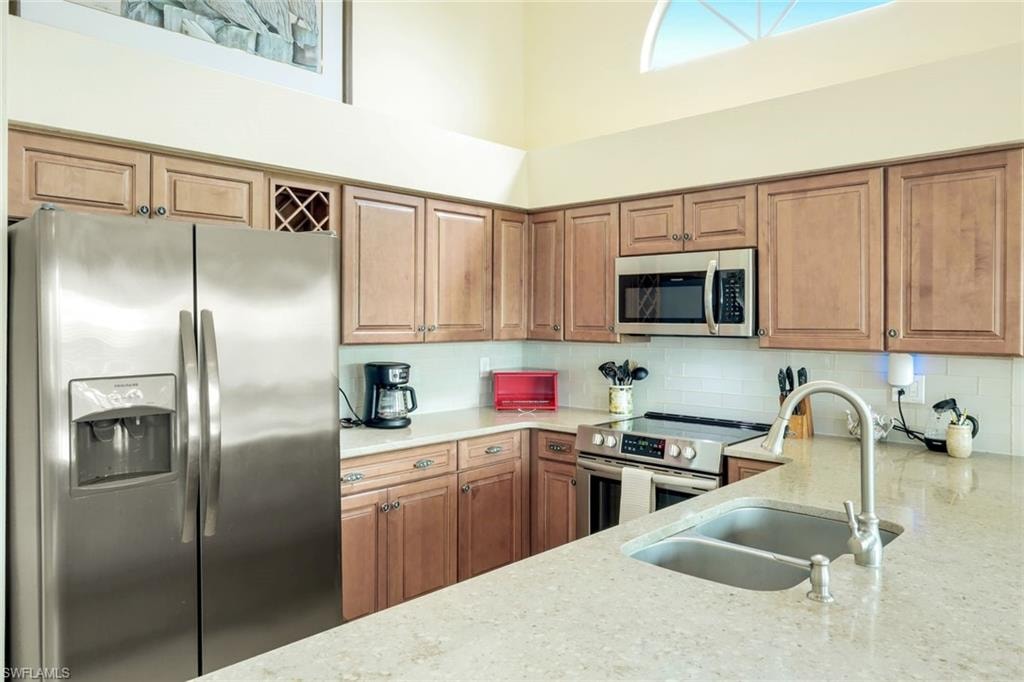 Kitchen featuring wood cabinetry, stainless steel appliances, light-toned countertops, tile backsplash, and a double basin sink with a gooseneck faucet
