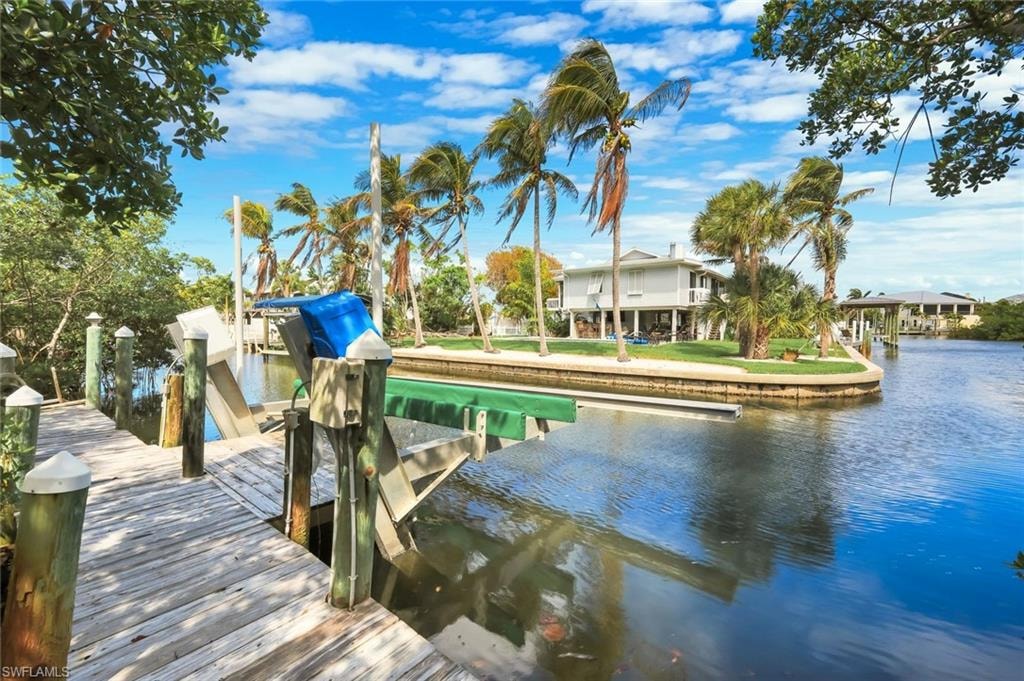 Dock with boat lift, waterfront access, and lush tropical landscaping