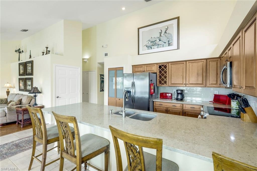 Kitchen featuring a large light-toned countertop island with an integrated double sink, wood cabinetry, a tile backsplash, and stainless steel appliances