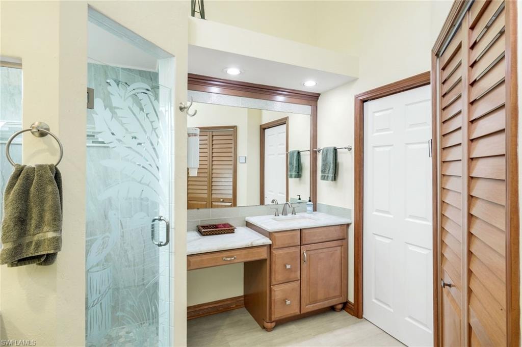 Frosted glass shower enclosure, single vanity with integrated sink, stone countertop, wood-finish cabinetry, and recessed lighting