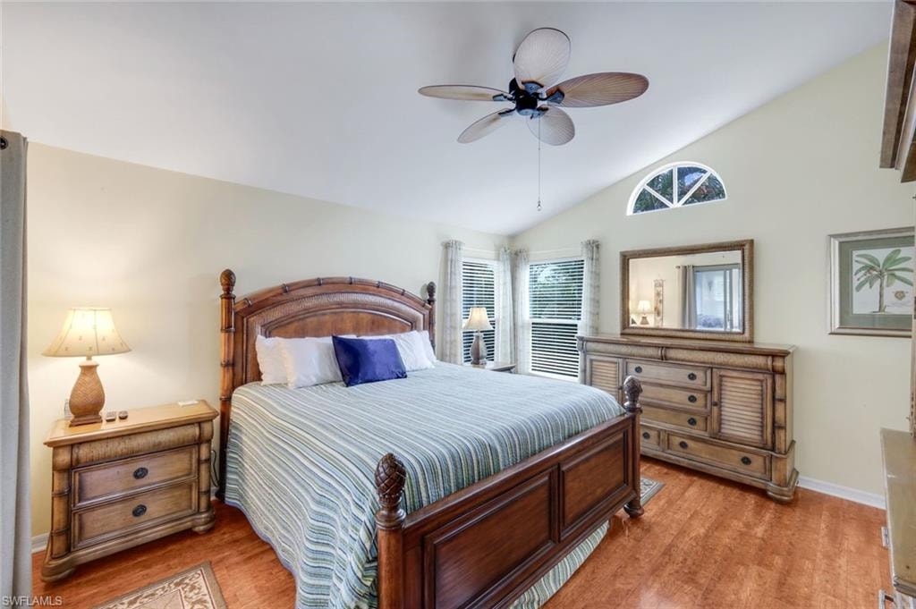 Vaulted ceiling with a ceiling fan, arched transom window, wood-finish flooring, and multiple windows with blinds