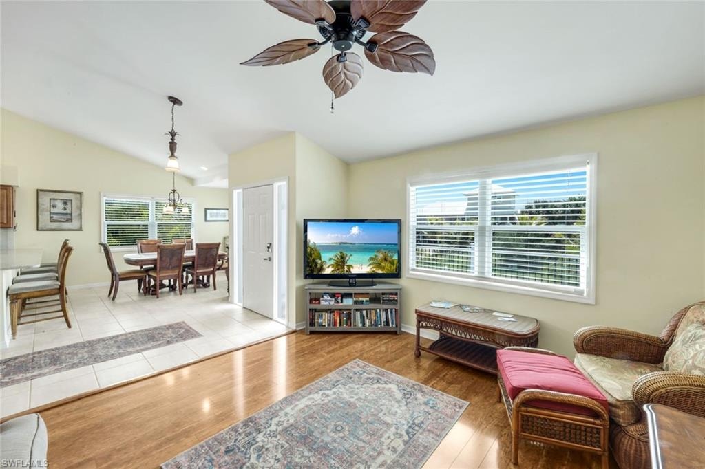 Bright and open living area showcasing wood-finish flooring, a ceiling fan with decorative blade detailing, and large windows with plantation shutters