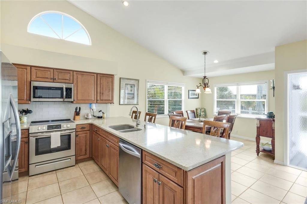 Vaulted ceiling with an arched window, stainless steel appliances, wood-finish cabinetry, light-toned countertops, and tile flooring