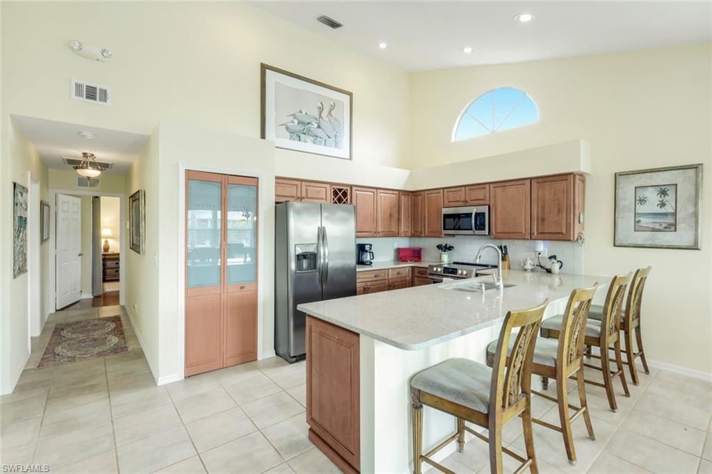 Kitchen featuring a peninsula island, stainless steel appliances, wood-finish cabinetry, and vaulted ceilings with an arched window