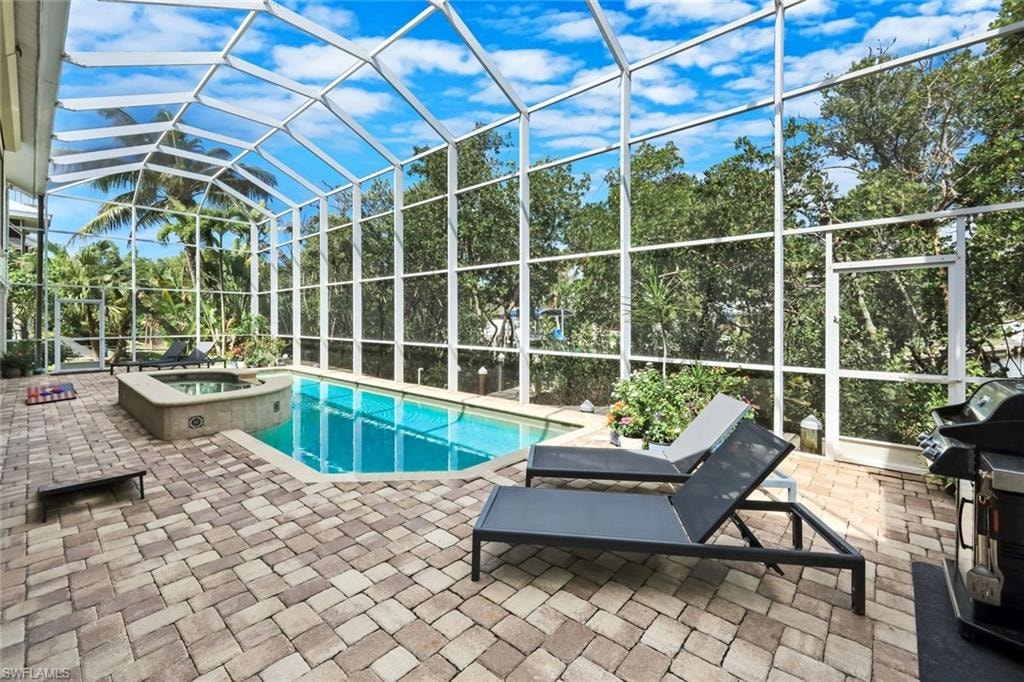 Screened enclosure featuring a geometric swimming pool with an integrated spa, and paver decking