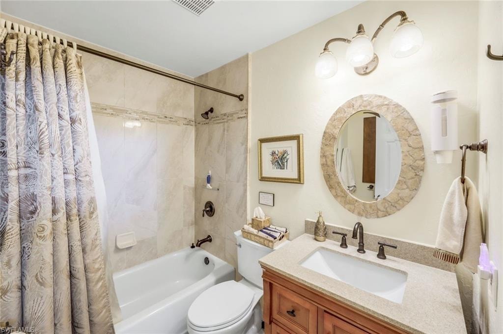 Full bathroom with a tub and shower combination featuring tiled walls, a vanity with a light-toned countertop, and a circular mirror