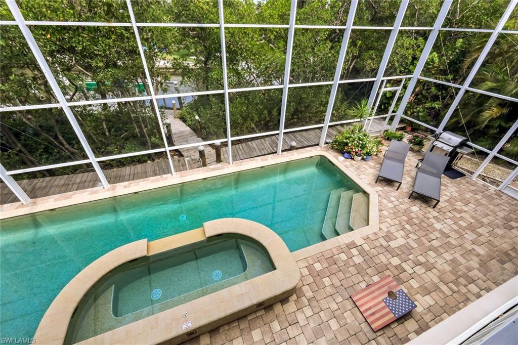 Screened pool enclosure featuring a rectangular pool with integrated spa and paver decking