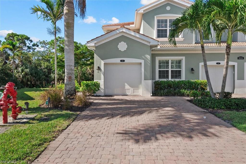 Paver driveway with lush landscaping, featuring a two-story exterior with a garage and double-pane windows
