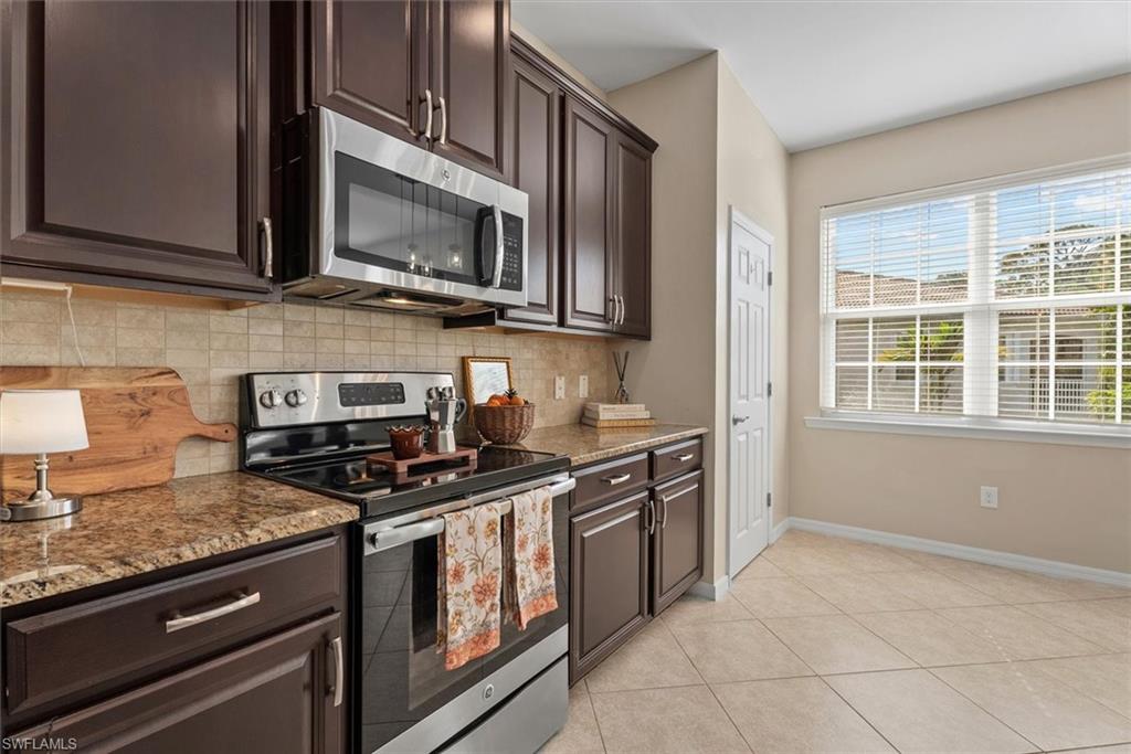 Dark wood cabinetry with stainless steel hardware, stainless steel appliances, stone-finish countertops, tiled backsplash, and tiled flooring