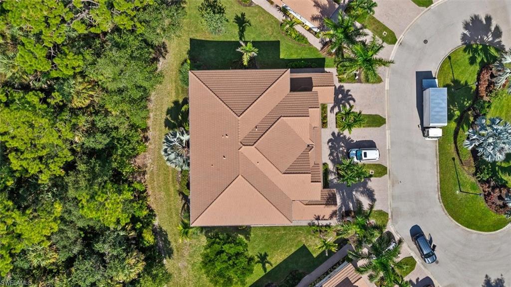 Terracotta-style tile roof, paver driveway, lush green landscaping, surrounding mature trees, and a cul-de-sac street