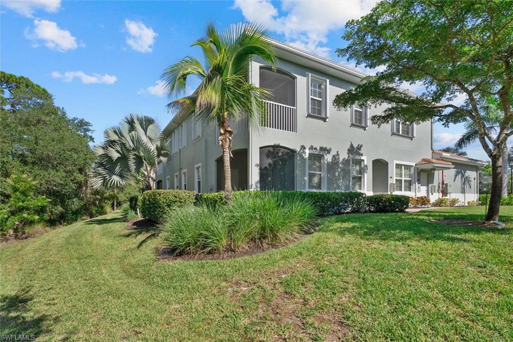 Two-story structure with a screened balcony, mature landscaping, and stucco exterior