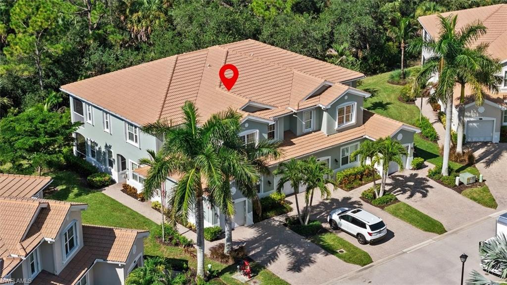 Two-story residence with a tile roof, light-colored exterior, multiple attached garages, and mature palm trees