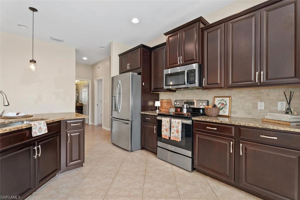Kitchen featuring dark wood cabinetry, stainless steel appliances, granite countertops, and tile flooring
