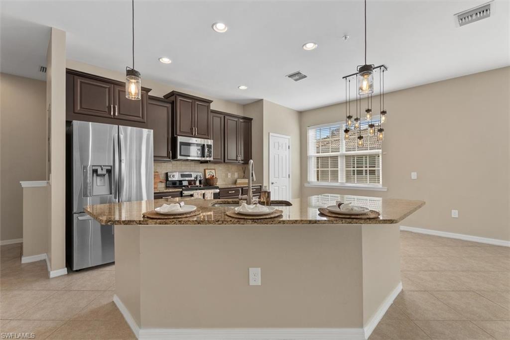 Kitchen featuring stainless steel appliances, dark wood-finish cabinetry, a large island with a stone-finish countertop, and recessed lighting