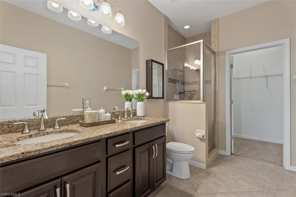 Spa-inspired primary bathroom featuring a dual-sink vanity with granite countertops, dark cabinetry with polished hardware, and a walk-in shower with frameless glass enclosure