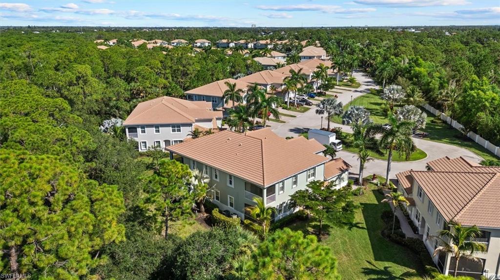 Community with tile-roofed buildings, lush green landscaping, paved roadways, and a tree-lined perimeter