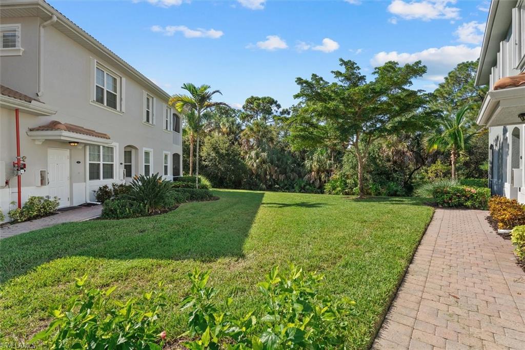 Stucco exterior with multiple windows, paver walkway, manicured lawn, and mature landscaping