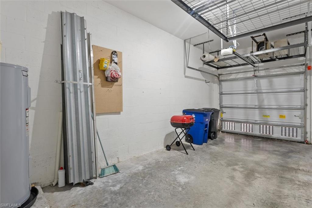 Concrete flooring, white painted block walls, overhead garage door, built-in overhead storage racks, and a water heater