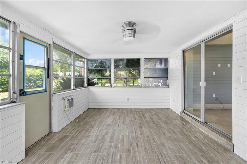 Enclosed patio featuring wood-finish flooring, white shiplap walls, multiple windows, a ceiling-mounted light fixture, and sliding glass doors